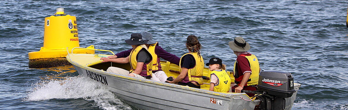 four adults and child in small boat wearing yellow life jackets